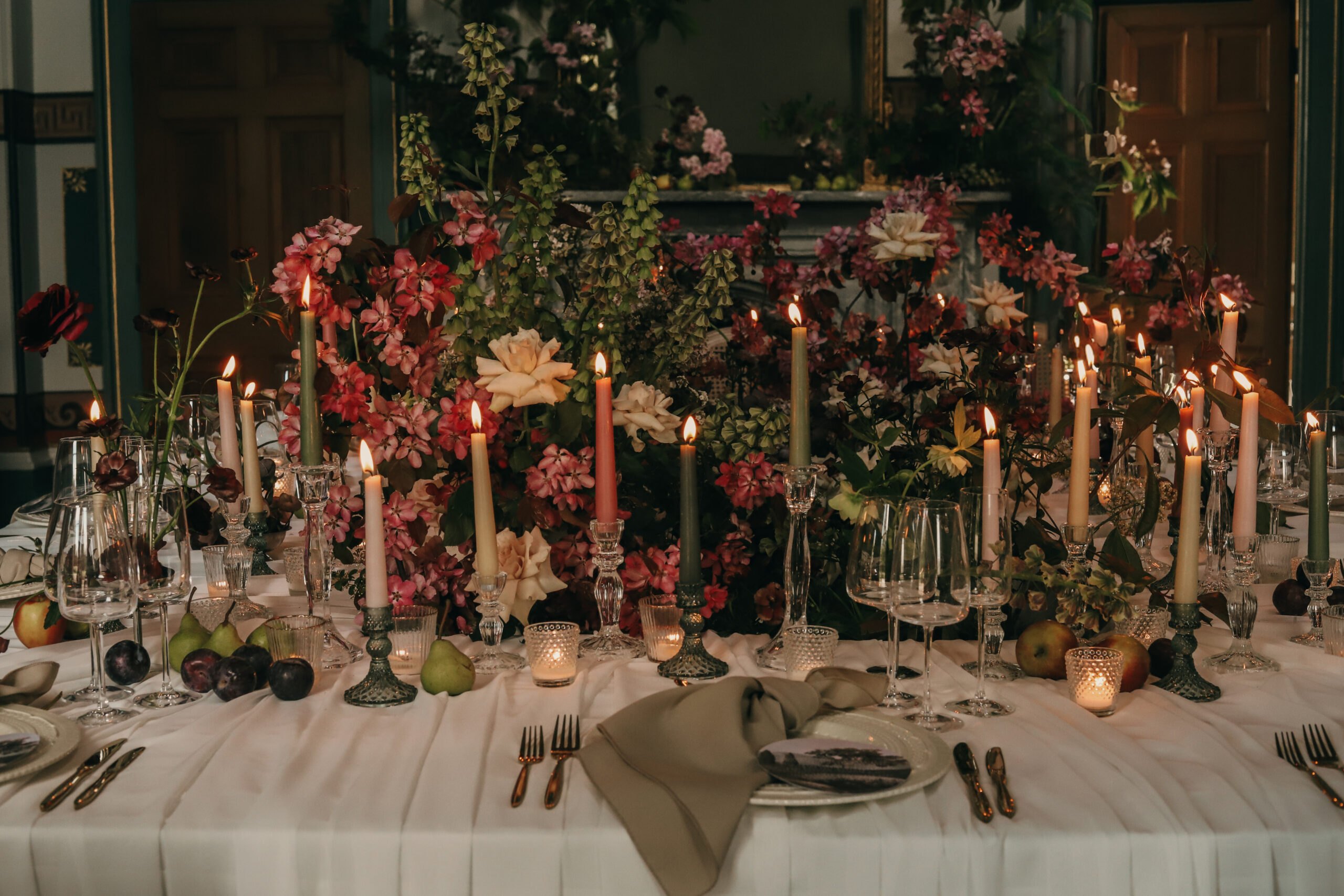 Candlelit wedding reception table with deep red florals and taper candles